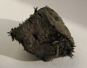 Ein dunkelgrauer, fast schwarzer Stein liegt ist zu sehen, der kleine Partikel magnetisch angezogen hat.